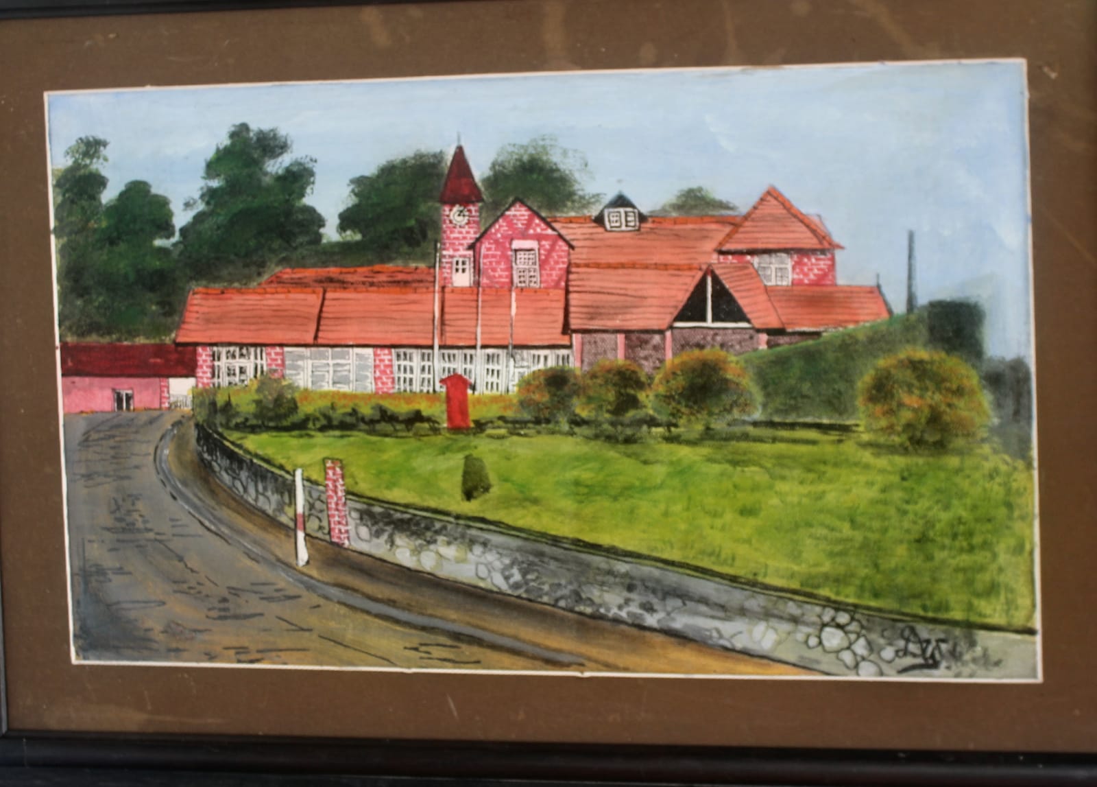 Painting of a colonial-style building with red tiled roofs and a clock tower beside a curving road and stone wall, in a brown mount